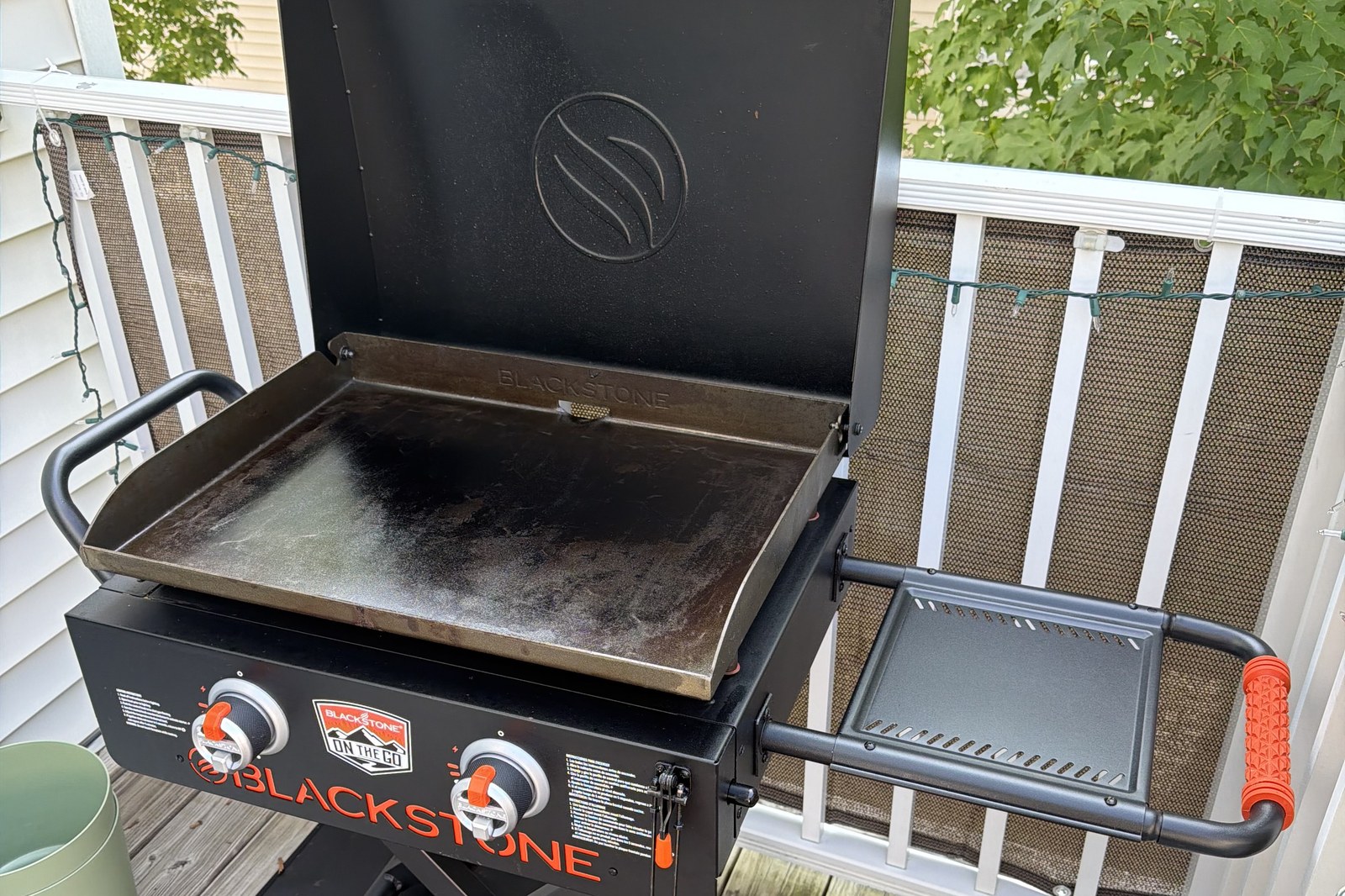 The same griddle with the hood open, showing a dark carbon steel plate with uneven patches of seasoning and a grease slot along the rear edge
