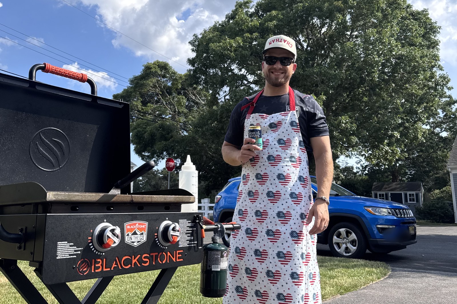 The griddle set up on a driveway beside a parked car, with a one pound propane cylinder screwed directly into its regulator