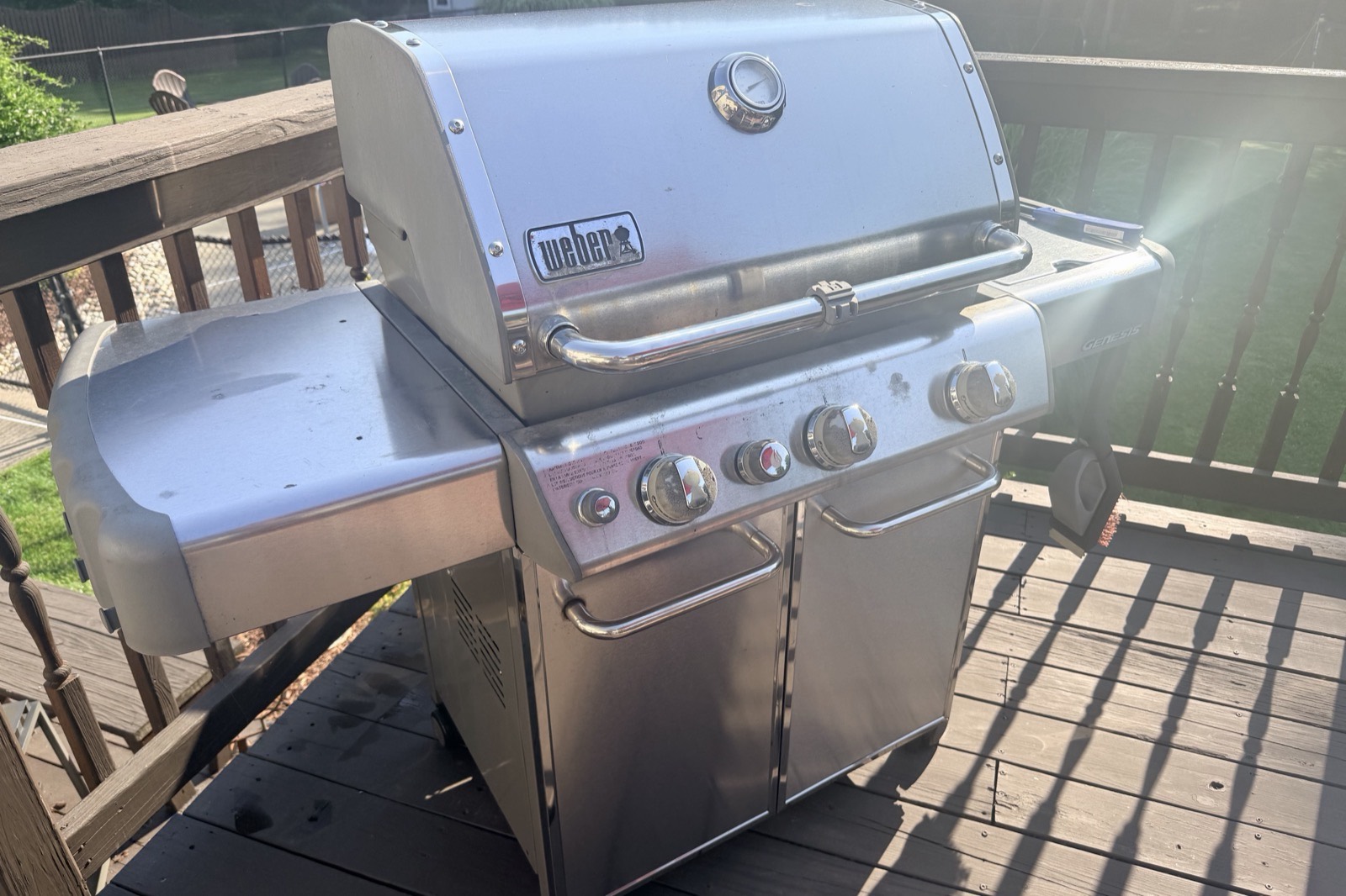 A stainless steel Weber gas grill on a wooden deck in low evening sunlight